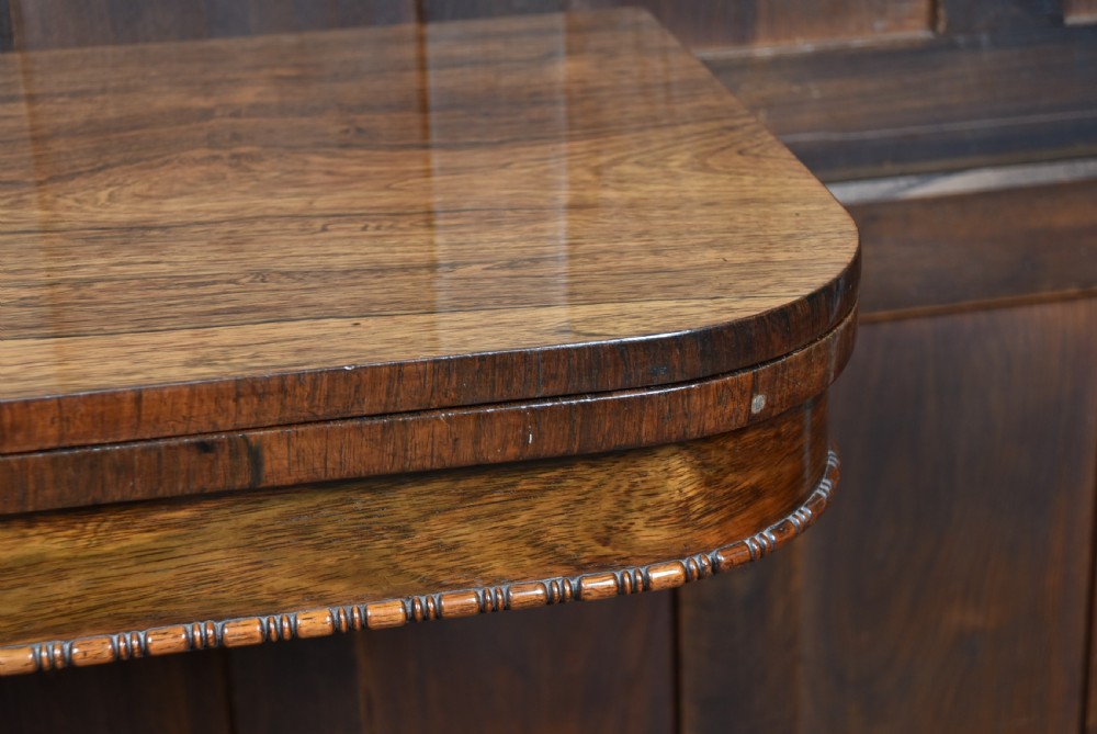 A Victorian rosewood fold-over games table featuring a polished rectangular top, turned carved pedestal stem, and a quadripartite plinth base with carved claw feet. View VII