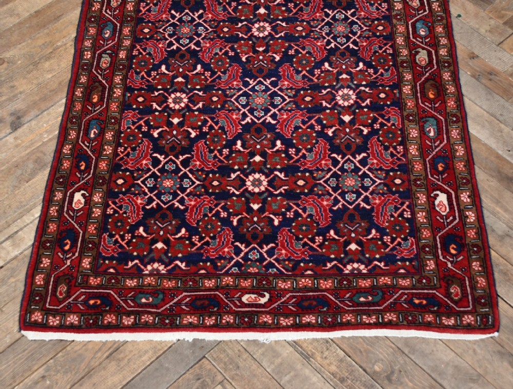 A rectangular hand-knotted wool Persian rug featuring a dark navy blue central field filled with intricate red floral lattice patterns and surrounded by decorative floral borders with short end fringe. View II