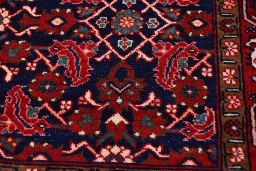 A rectangular hand-knotted wool Persian rug featuring a dark navy blue central field filled with intricate red floral lattice patterns and surrounded by decorative floral borders with short end fringe. View VI