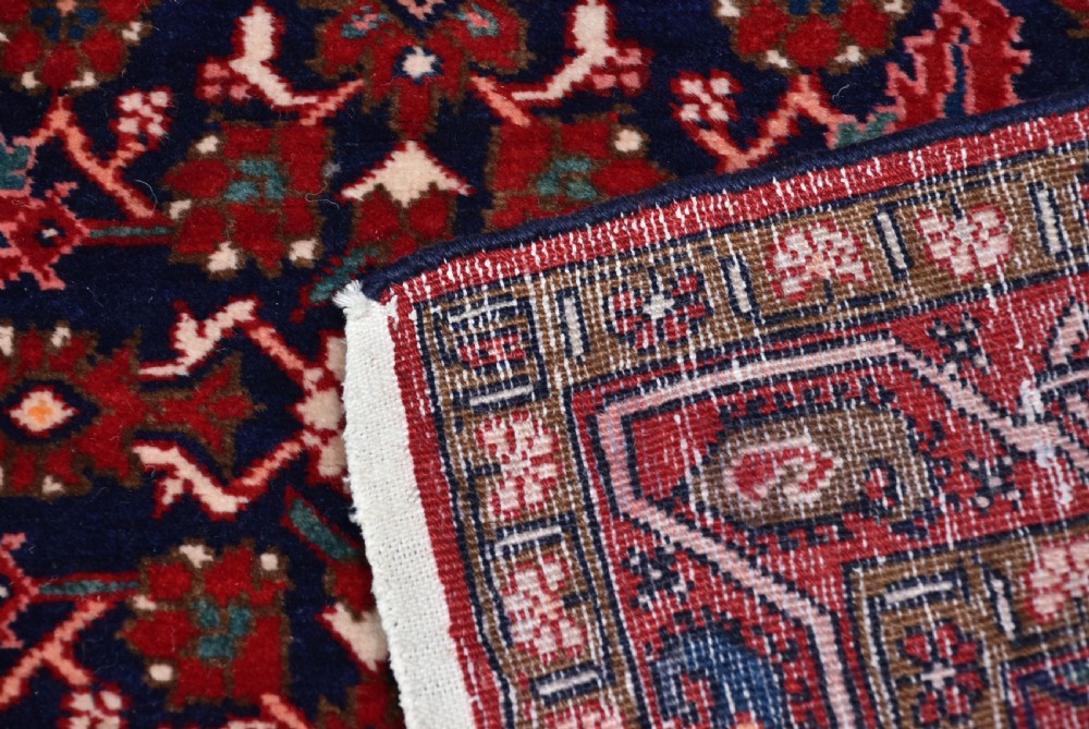 A rectangular hand-knotted wool Persian rug featuring a dark navy blue central field filled with intricate red floral lattice patterns and surrounded by decorative floral borders with short end fringe. View VIII