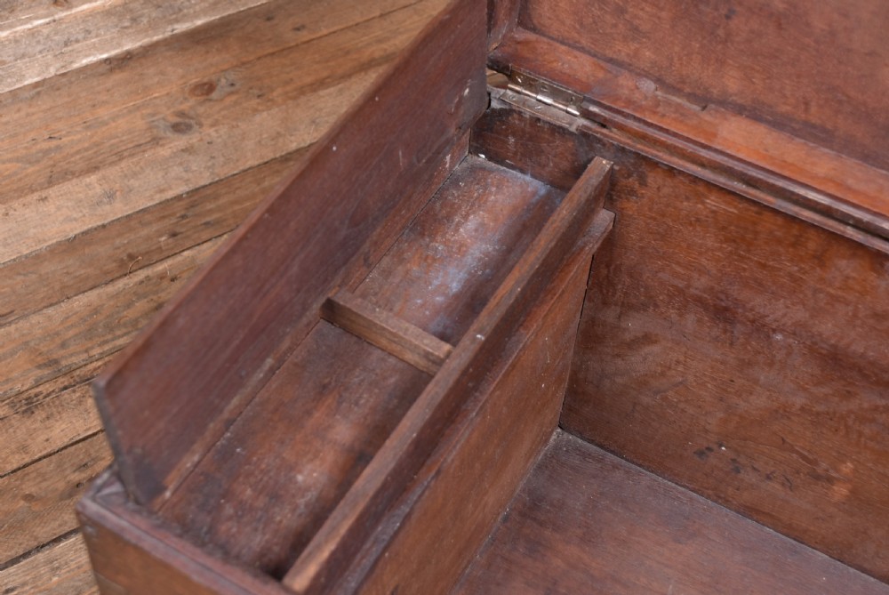 A 19th-century dark teak storage chest featuring detailed relief carving of figures and architecture on the front and side panels, complete with brass latches and corner straps. View XVI