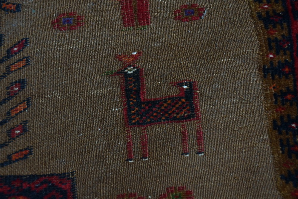 A handwoven vintage Iranian rug featuring a light brown central field decorated with animal and bird motifs framed by dark red geometric borders. View X