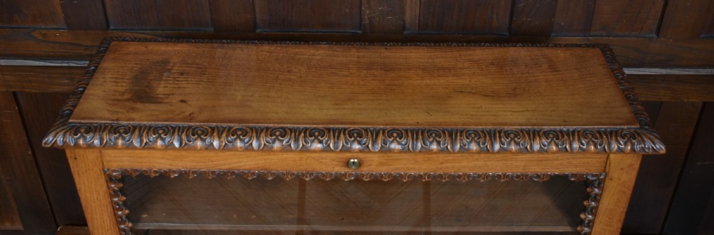 A Victorian oak counter-top display cabinet featuring carved border trim, interior wooden shelves, a glazed front, and a top brass keyhole. View IX