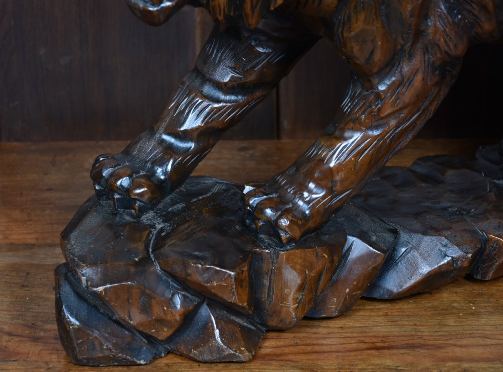 A carved dark wood sculpture depicting a roaring tiger with open jaws and detailed striped fur, resting on an integrated rocky base. View III
