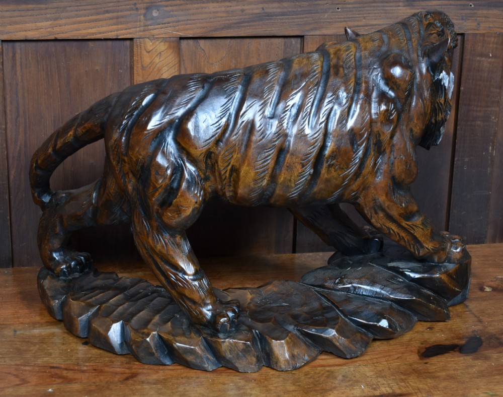A carved dark wood sculpture depicting a roaring tiger with open jaws and detailed striped fur, resting on an integrated rocky base. View IX