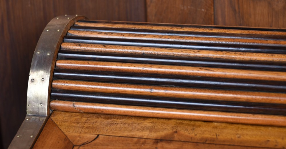 A nineteenth-century camphor wood roll-top writing box with brass-bound corners, a central brass cartouche, and a slatted tambour top. View VI