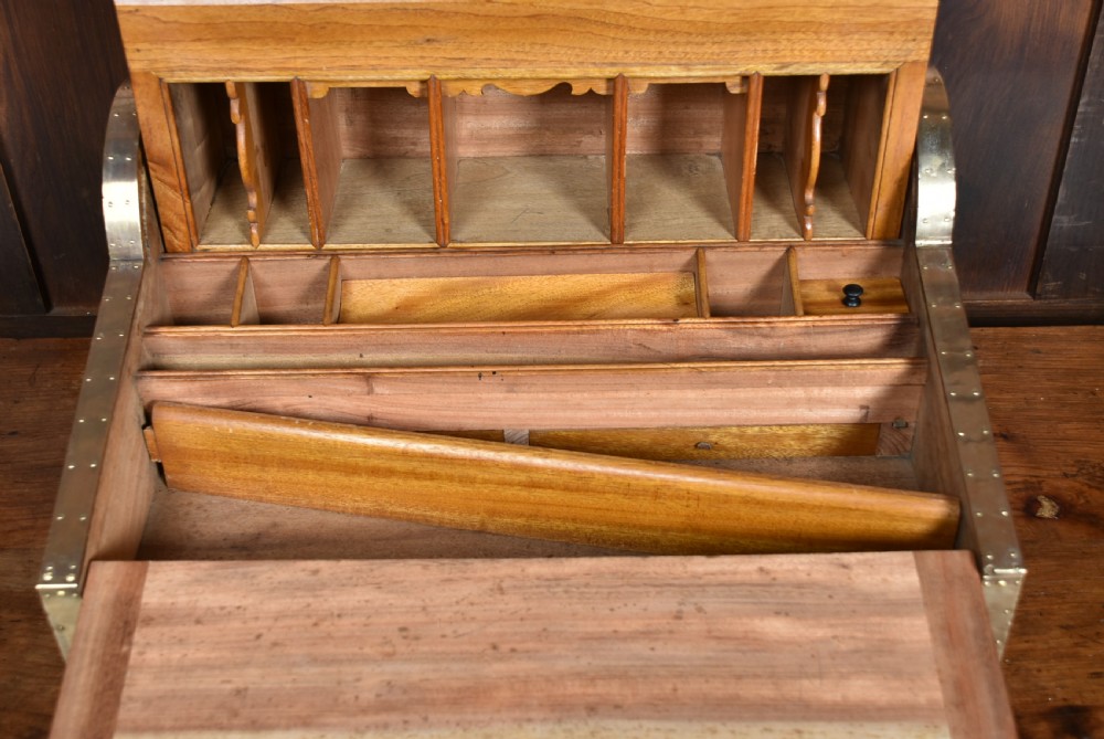 A nineteenth-century camphor wood roll-top writing box with brass-bound corners, a central brass cartouche, and a slatted tambour top. View XV