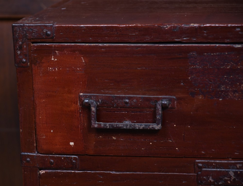 A Japanese dark red lacquered wood tansu chest featuring heavy iron corner mounts, bail handles, and multiple drawers of varying sizes. View VIII