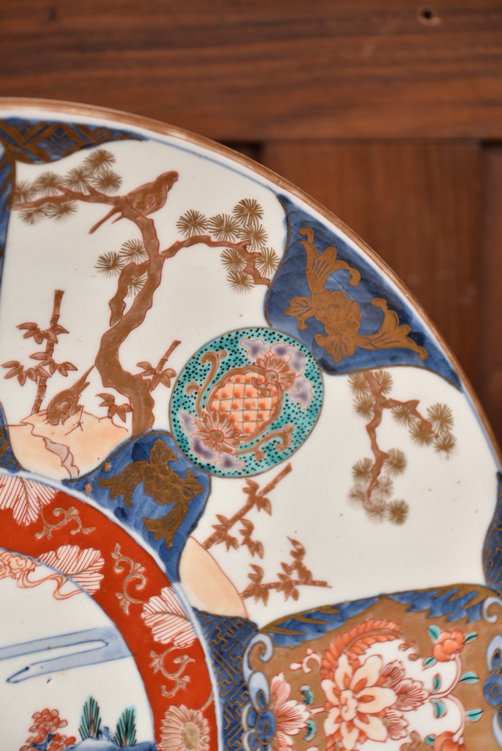 A decorated circular Japanese Imari porcelain charger with blue, red, and gold floral and landscape motifs, resting inside a square wooden storage box alongside its lid. View VIII