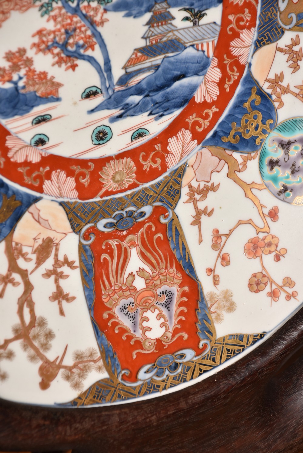 A decorated circular Japanese Imari porcelain charger with blue, red, and gold floral and landscape motifs, resting inside a square wooden storage box alongside its lid. View IX