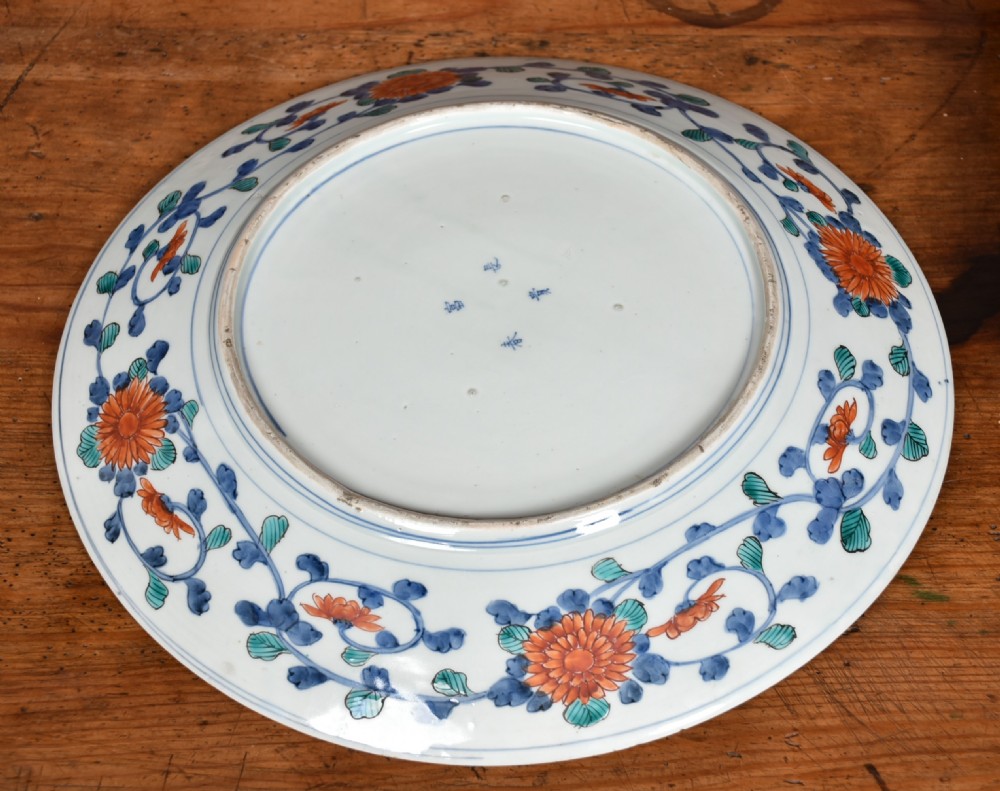 A decorated circular Japanese Imari porcelain charger with blue, red, and gold floral and landscape motifs, resting inside a square wooden storage box alongside its lid. View X