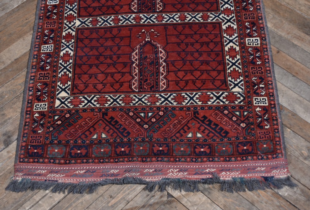 A handwoven red wool rug featuring double arched niche motifs, geometric border patterns, dark navy details, and fringe ends. View III