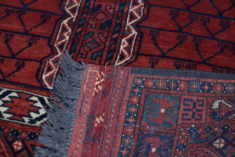 A handwoven red wool rug featuring double arched niche motifs, geometric border patterns, dark navy details, and fringe ends. View VII
