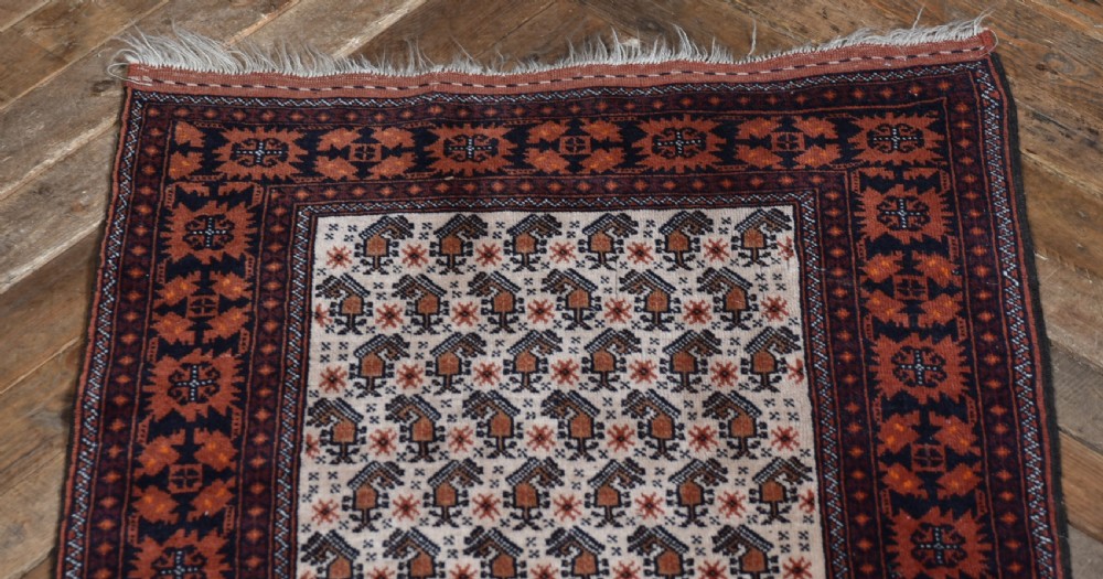 A hand-woven wool rug featuring a cream central field with repeating geometric motifs surrounded by a wide rust-red patterned border and white fringe. View II