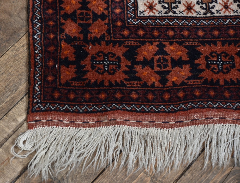 A hand-woven wool rug featuring a cream central field with repeating geometric motifs surrounded by a wide rust-red patterned border and white fringe. View VIII