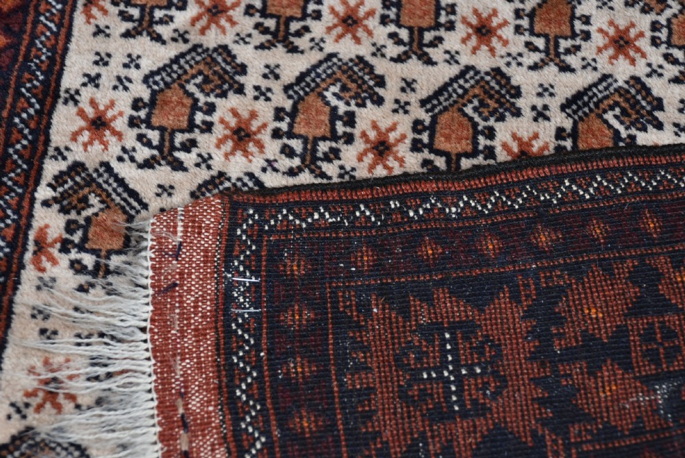 A hand-woven wool rug featuring a cream central field with repeating geometric motifs surrounded by a wide rust-red patterned border and white fringe. View IX