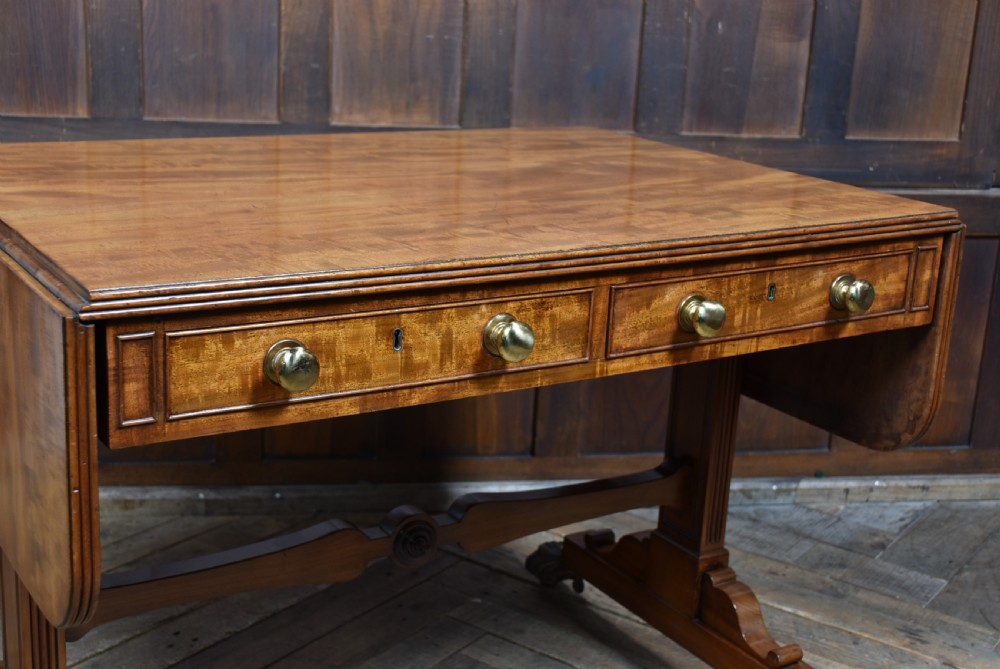 A Regency mahogany drop-leaf sofa table featuring flame mahogany drawer fronts, reeded upright trestle legs, a stretcher with central roundel, and brass lion paw castors. View V
