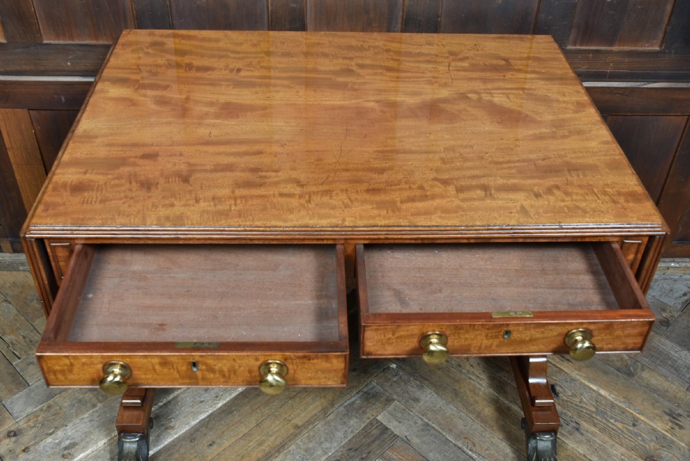 A Regency mahogany drop-leaf sofa table featuring flame mahogany drawer fronts, reeded upright trestle legs, a stretcher with central roundel, and brass lion paw castors. View XIII