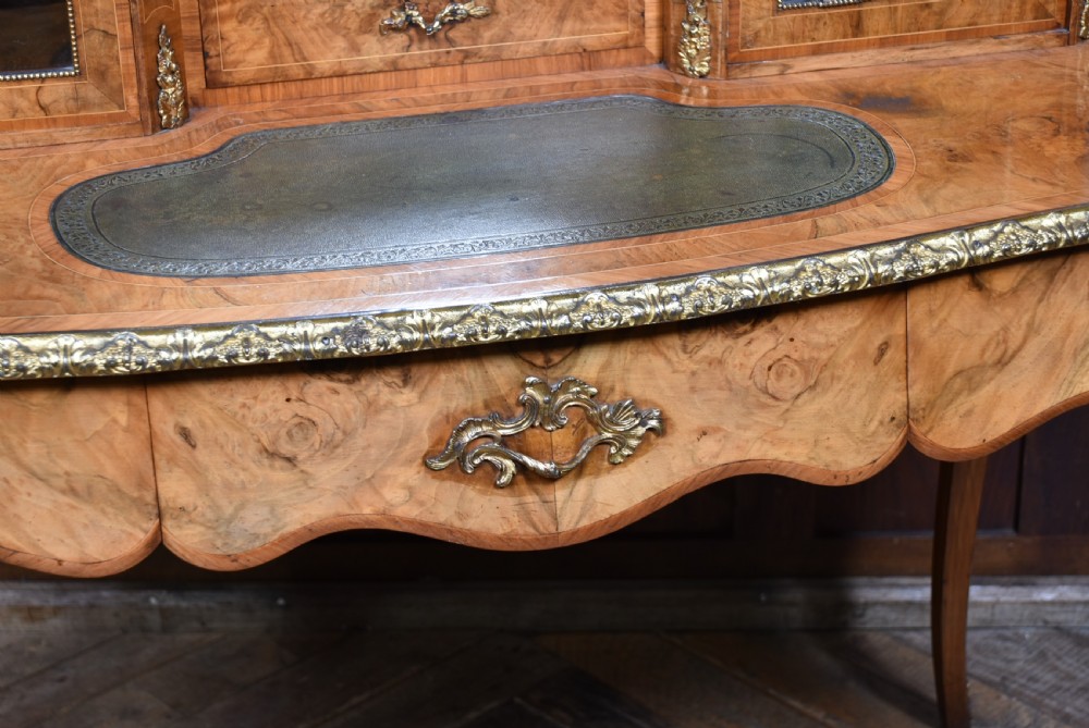 Victorian burr walnut writing desk featuring cabriole legs, brass mounts, an inset leather writing top, and an upper superstructure with glazed side cabinets and a central mirror. View V
