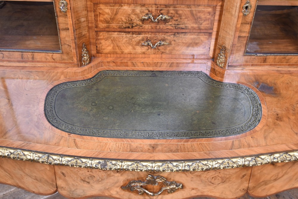 Victorian burr walnut writing desk featuring cabriole legs, brass mounts, an inset leather writing top, and an upper superstructure with glazed side cabinets and a central mirror. View VI