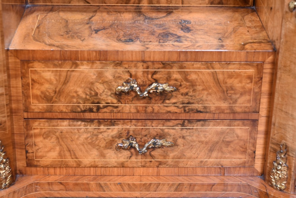 Victorian burr walnut writing desk featuring cabriole legs, brass mounts, an inset leather writing top, and an upper superstructure with glazed side cabinets and a central mirror. View VII