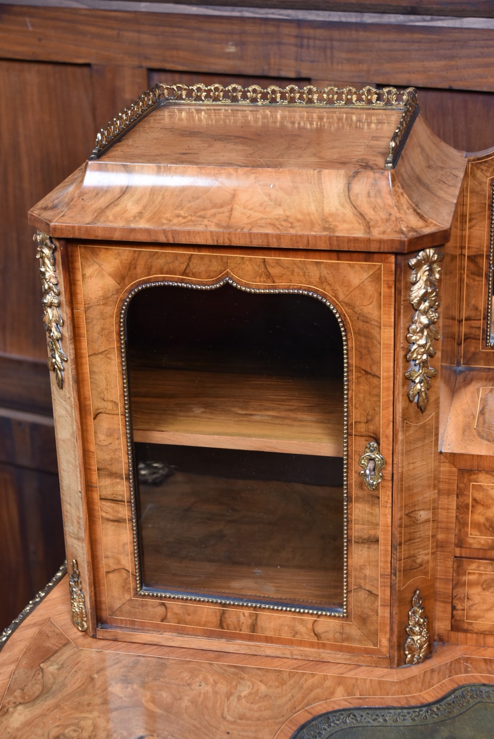 Victorian burr walnut writing desk featuring cabriole legs, brass mounts, an inset leather writing top, and an upper superstructure with glazed side cabinets and a central mirror. View X