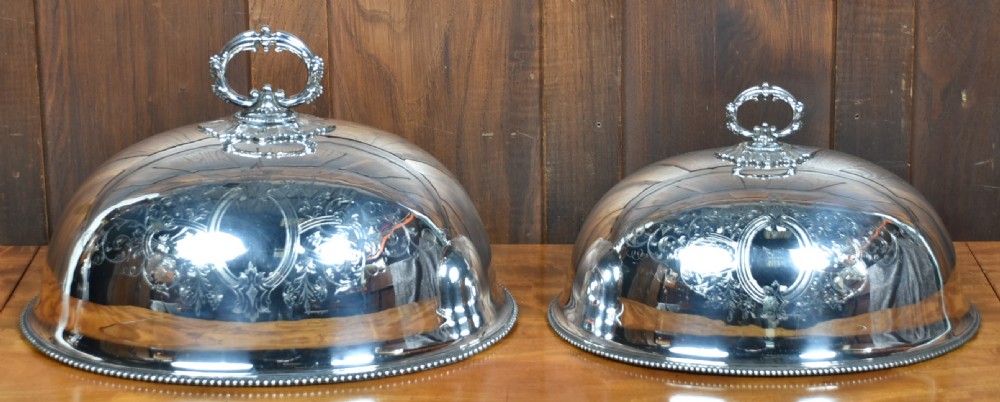 A pair of domed silver-plated meat covers featuring ornate cast handles, beaded lower rims, and engraved foliate cartouches. View II
