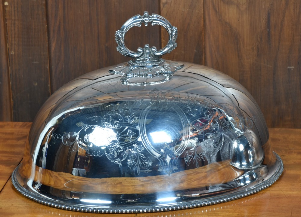 A pair of domed silver-plated meat covers featuring ornate cast handles, beaded lower rims, and engraved foliate cartouches. View III