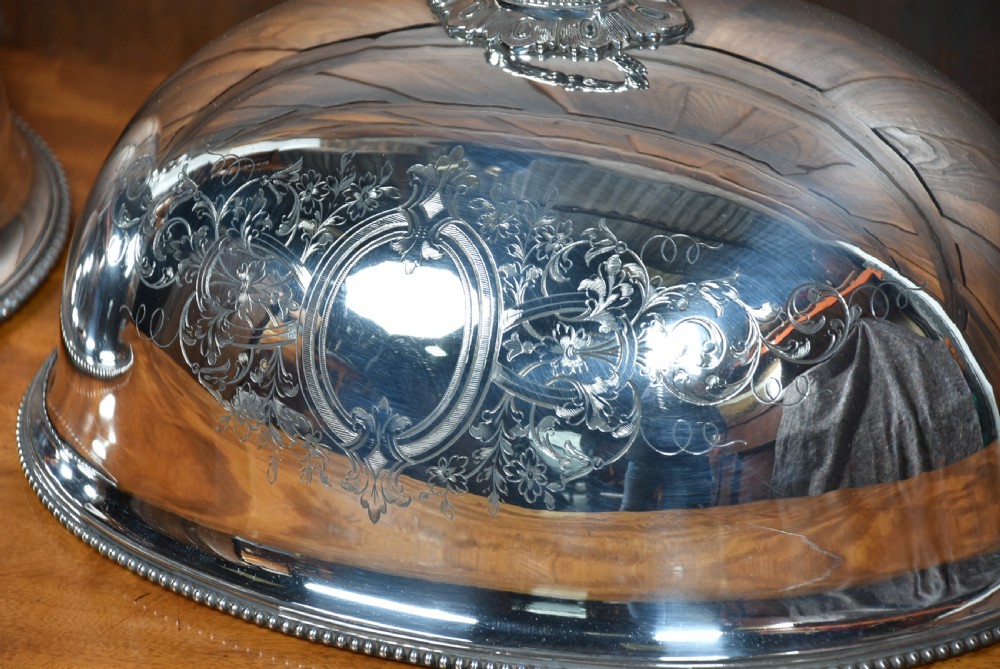 A pair of domed silver-plated meat covers featuring ornate cast handles, beaded lower rims, and engraved foliate cartouches. View VIII