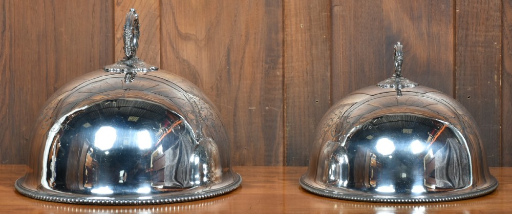 A pair of domed silver-plated meat covers featuring ornate cast handles, beaded lower rims, and engraved foliate cartouches. View IX