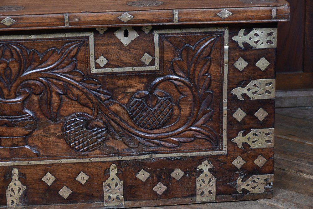 A low rectangular carved wood storage chest featuring decorative brass mounts, corner brackets, studs, and a central relief carving of a floral motif. View VIII