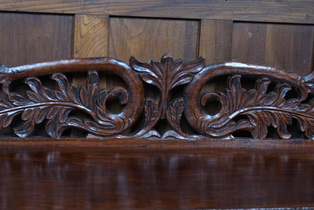 A carved dark padouk wood Anglo-Indian sideboard featuring an ornate foliage gallery top, carved frieze drawers, and two sunburst pedestal doors on turned bun feet. View V