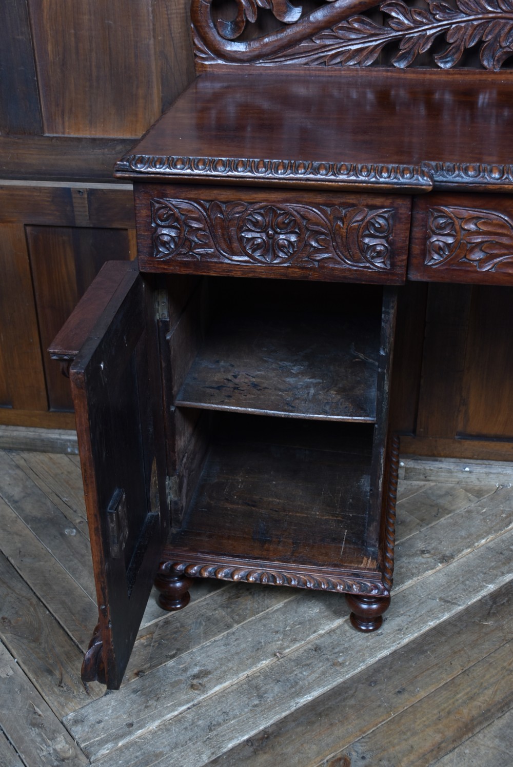A carved dark padouk wood Anglo-Indian sideboard featuring an ornate foliage gallery top, carved frieze drawers, and two sunburst pedestal doors on turned bun feet. View IX