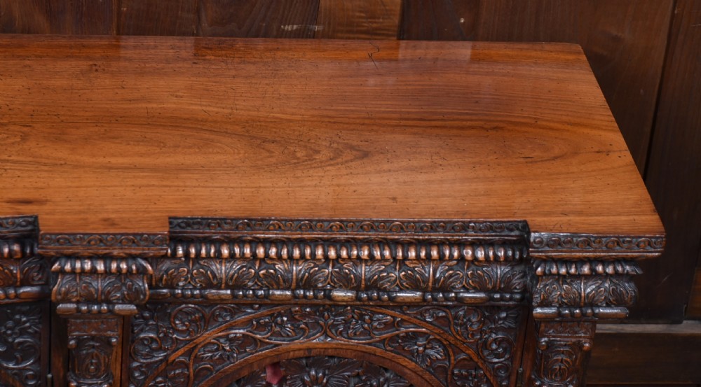 An Anglo-Indian dark padouk wood sideboard featuring intricate pierced openwork floral carvings across three arched cabinet doors and carved feet. View V