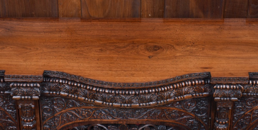 An Anglo-Indian dark padouk wood sideboard featuring intricate pierced openwork floral carvings across three arched cabinet doors and carved feet. View VI