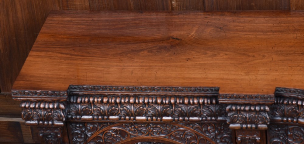 An Anglo-Indian dark padouk wood sideboard featuring intricate pierced openwork floral carvings across three arched cabinet doors and carved feet. View VII