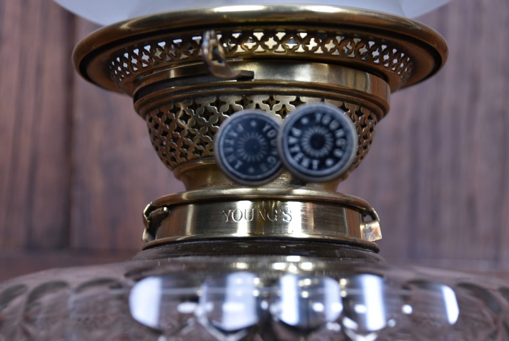A Victorian paraffin lamp featuring a stepped brass base, a diamond-cut crystal column topped with a brass Corinthian capital, a crystal reservoir, double wick knobs, and an etched frosted glass shade with a ruffled rim. View V