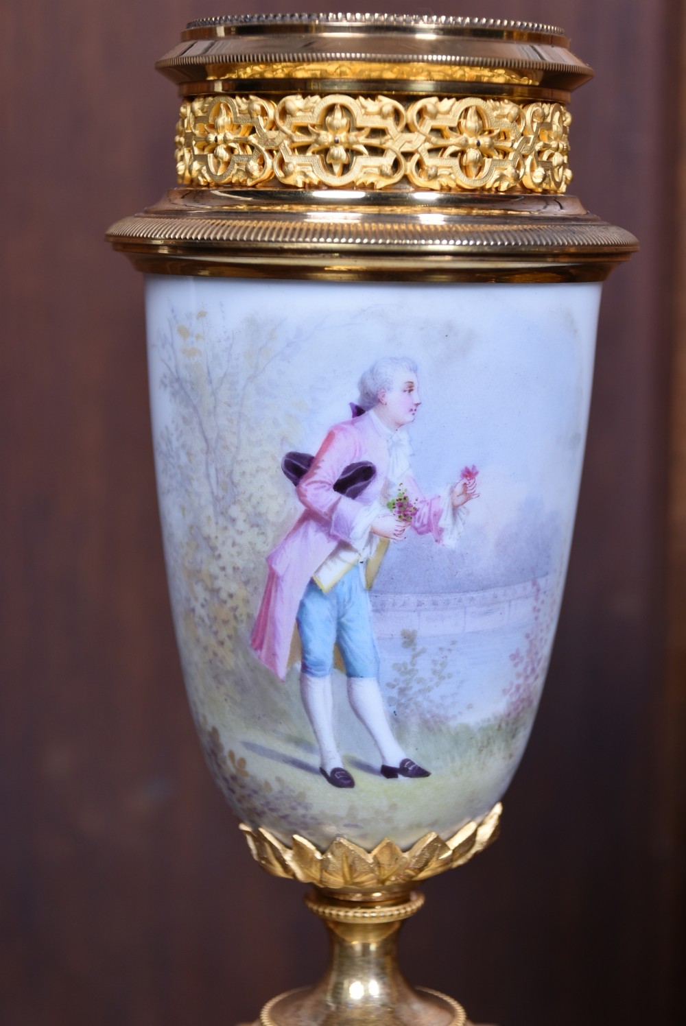 A three-piece antique French gilt metal and painted porcelain clock garniture set with matching side urns, each housed under a glass dome on a black base. View XVIII