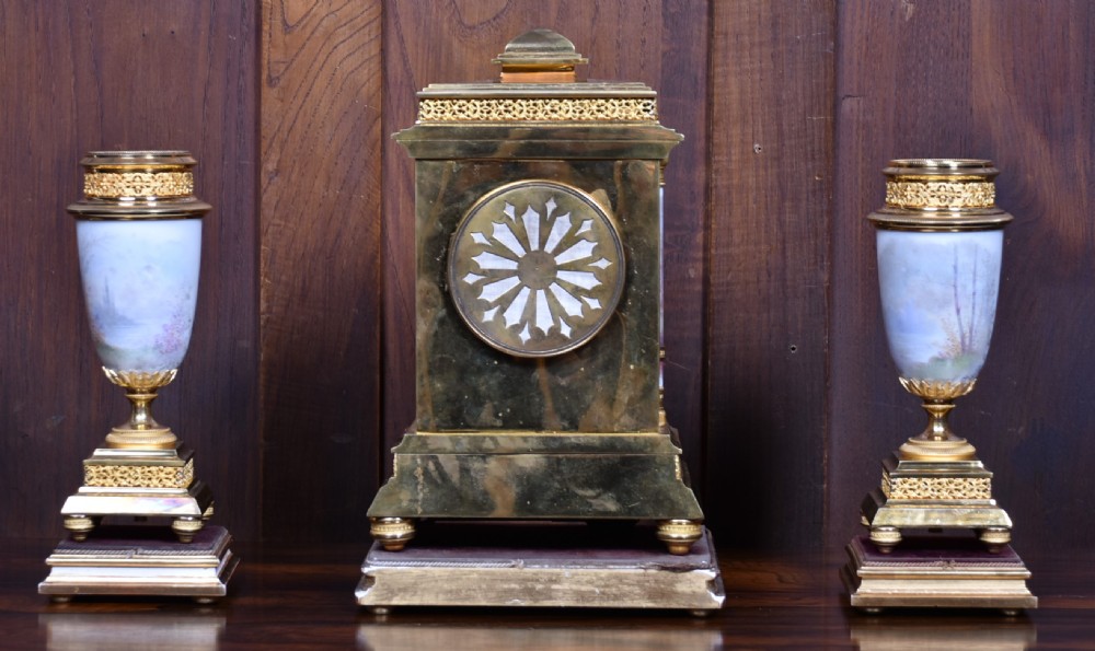 A three-piece antique French gilt metal and painted porcelain clock garniture set with matching side urns, each housed under a glass dome on a black base. View XXIII