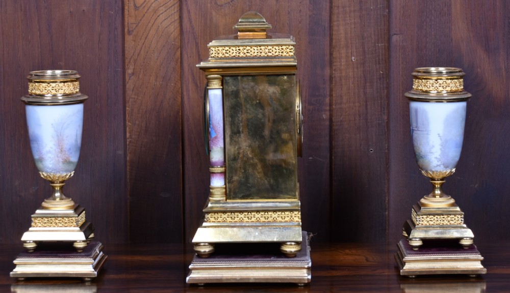 A three-piece antique French gilt metal and painted porcelain clock garniture set with matching side urns, each housed under a glass dome on a black base. View XXV