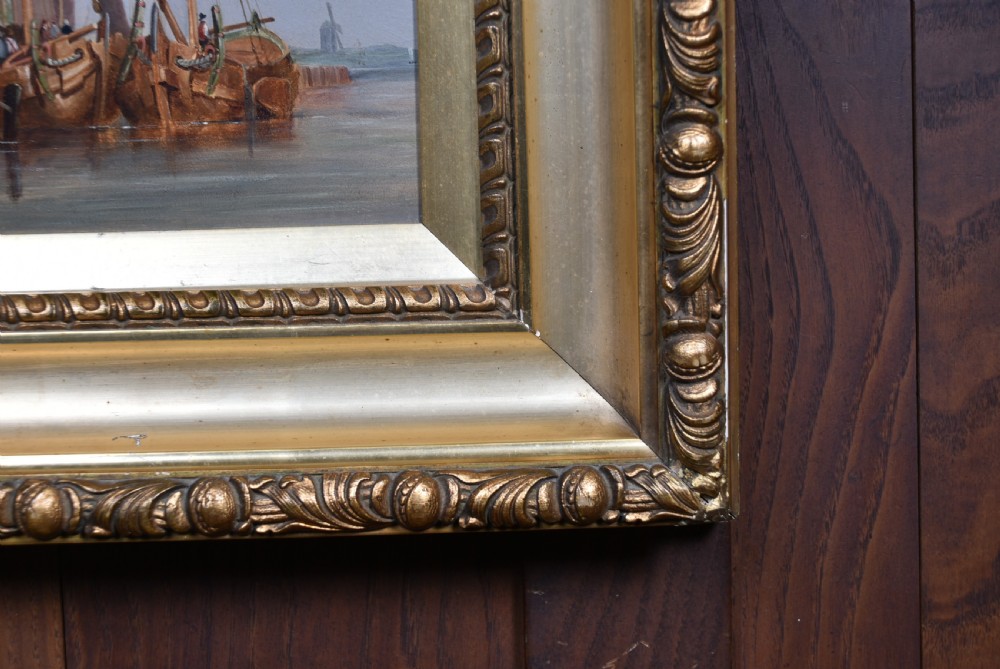 A framed oil painting depicting sailboats in a Dutch harbour beside historic brick buildings under a cloudy sky. View XI