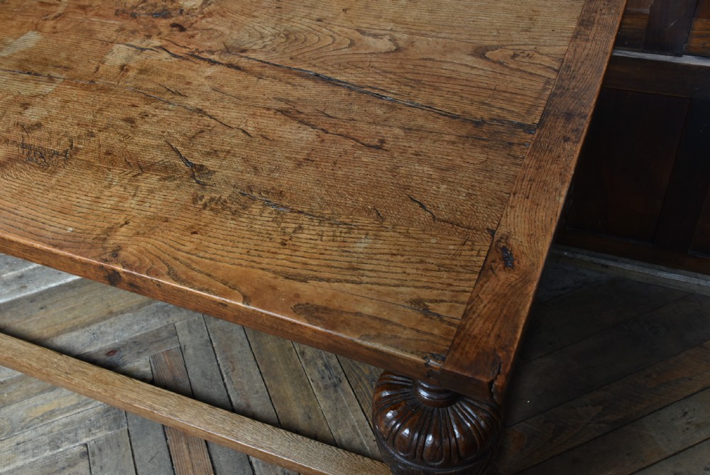 An 18th-century solid oak refectory table featuring a plank top and carved bulbous cup-and-cover turned legs resting on a stretcher base. View VII