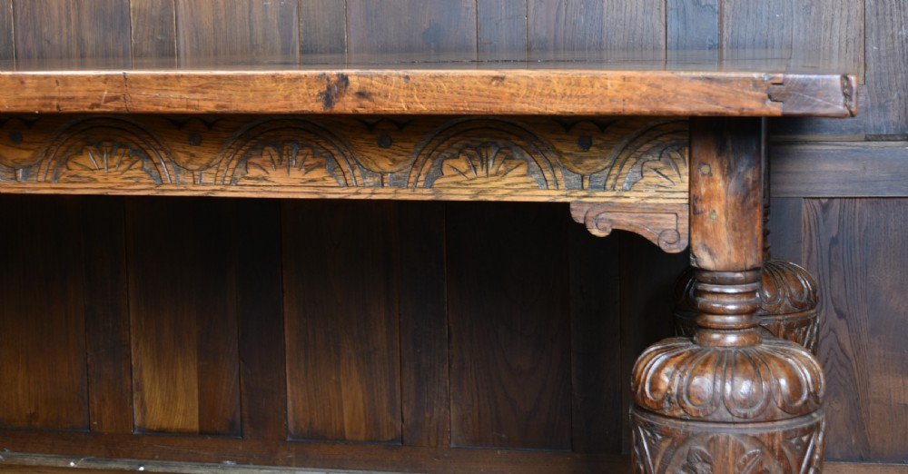 An 18th-century solid oak refectory table featuring a plank top and carved bulbous cup-and-cover turned legs resting on a stretcher base. View XII