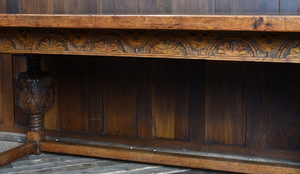 An 18th-century solid oak refectory table featuring a plank top and carved bulbous cup-and-cover turned legs resting on a stretcher base. View XIII