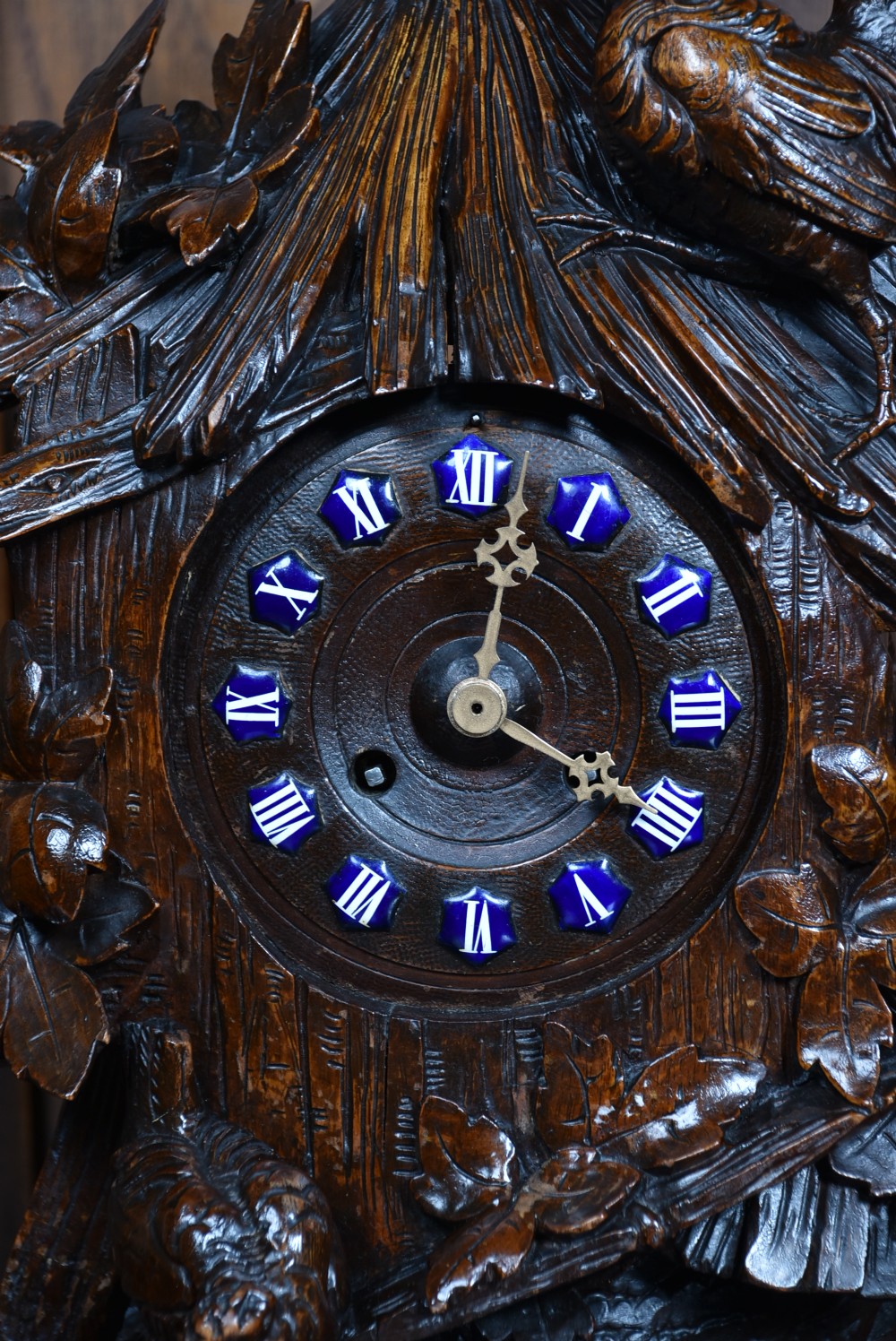 A hand-carved wooden mantel clock featuring a cockerel finial, foliage motifs, and a central dial with blue enamel Roman numeral cartouches. View II