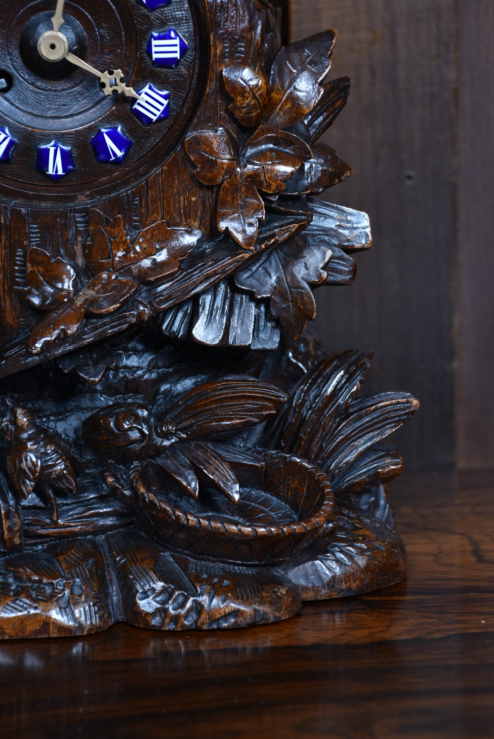 A hand-carved wooden mantel clock featuring a cockerel finial, foliage motifs, and a central dial with blue enamel Roman numeral cartouches. View VII
