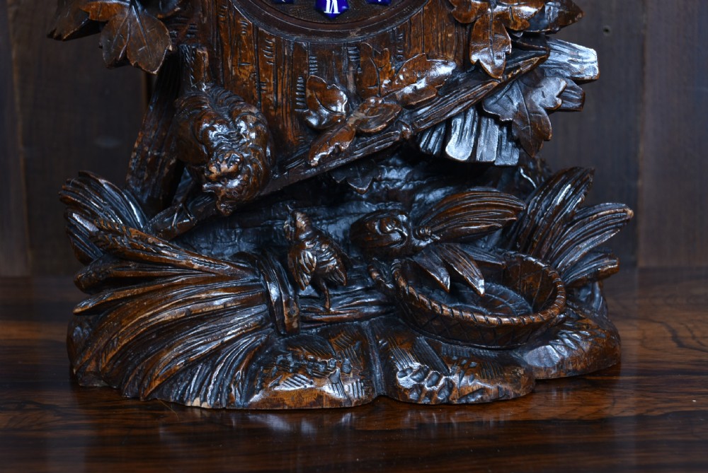 A hand-carved wooden mantel clock featuring a cockerel finial, foliage motifs, and a central dial with blue enamel Roman numeral cartouches. View VIII