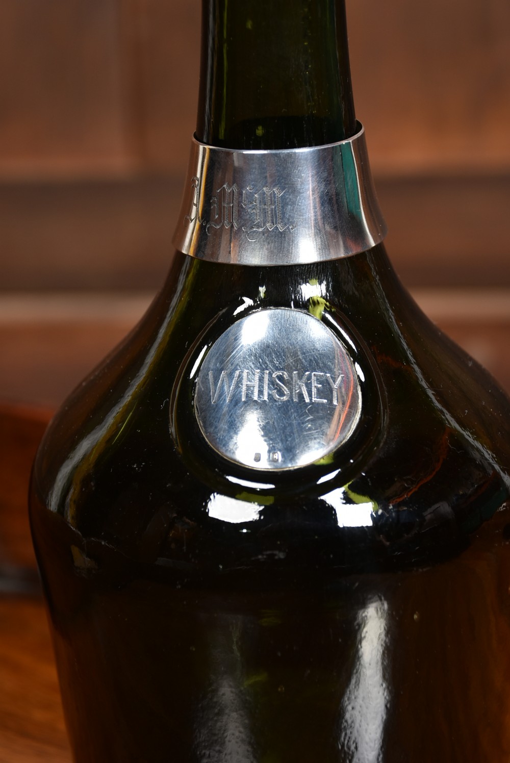 A dark green glass decanter featuring silver collar band, silver ball stopper, and a silver oval plaque engraved with WHISKEY. View V