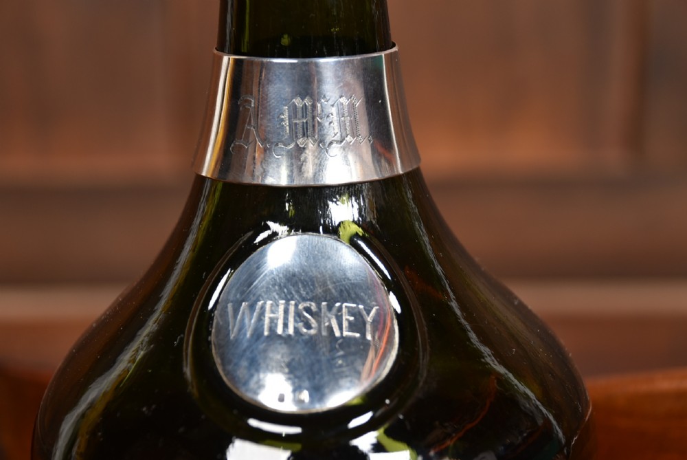 A dark green glass decanter featuring silver collar band, silver ball stopper, and a silver oval plaque engraved with WHISKEY. View VI