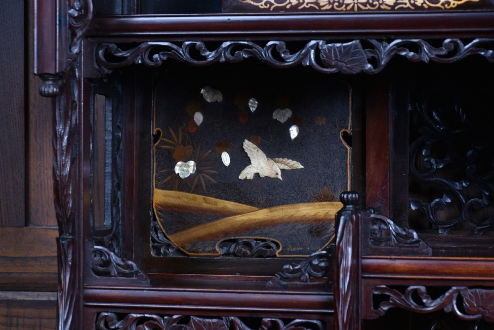A tall Japanese Meiji period dark hardwood shodana cabinet featuring asymmetrical shelving, mother-of-pearl inlaid panels, bird carvings, and a cresting pediment. View XIII